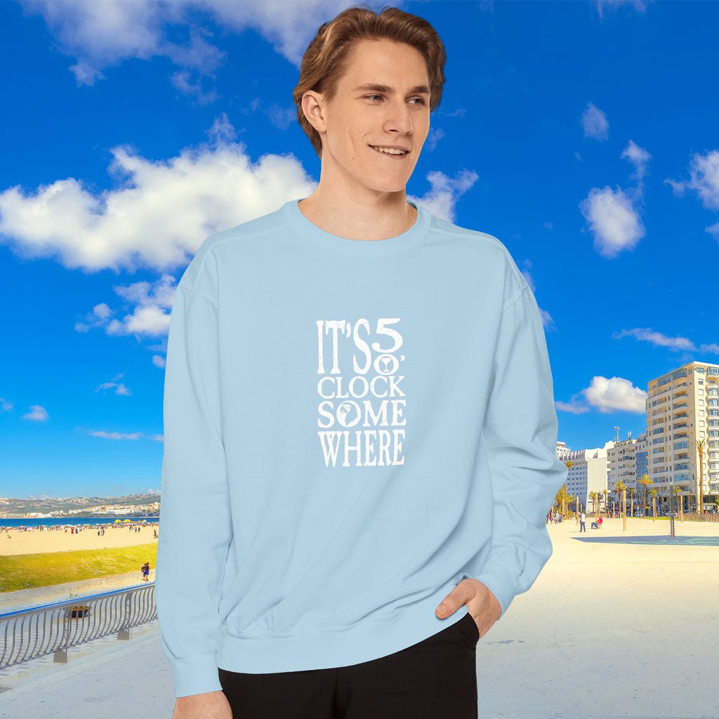 Person wearing a light blue sweatshirt with text, standing in front of a beach and buildings.