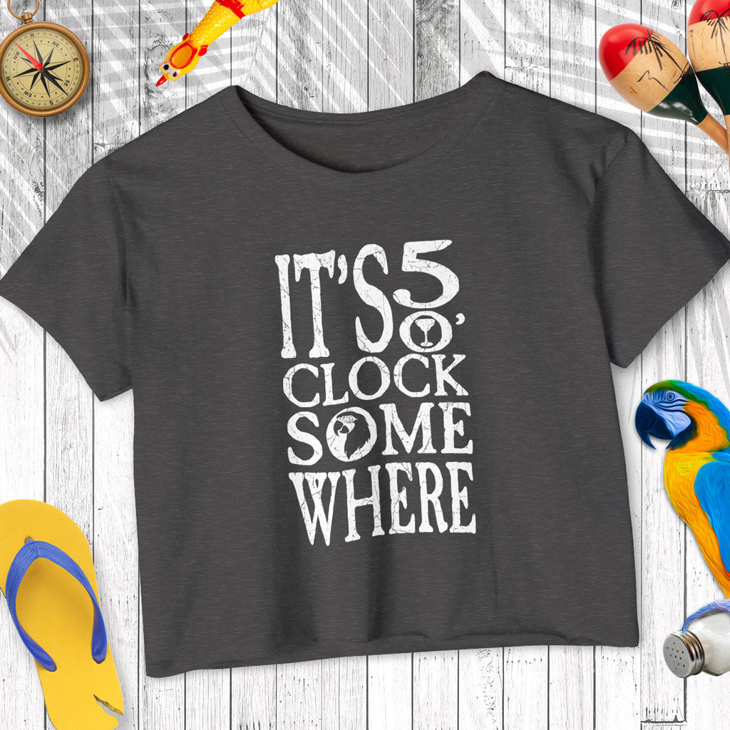 Black t-shirt with 'It's 5 o'clock somewhere' text on a wooden surface with decorative items.