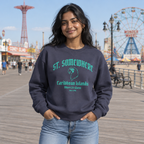 A woman stands on a boardwalk wearing a navy crewneck sweatshirt with a teal graphic that reads 'ST. SOMEWHERE Caribbean Islands Here I'll Bearn' and light blue jeans.