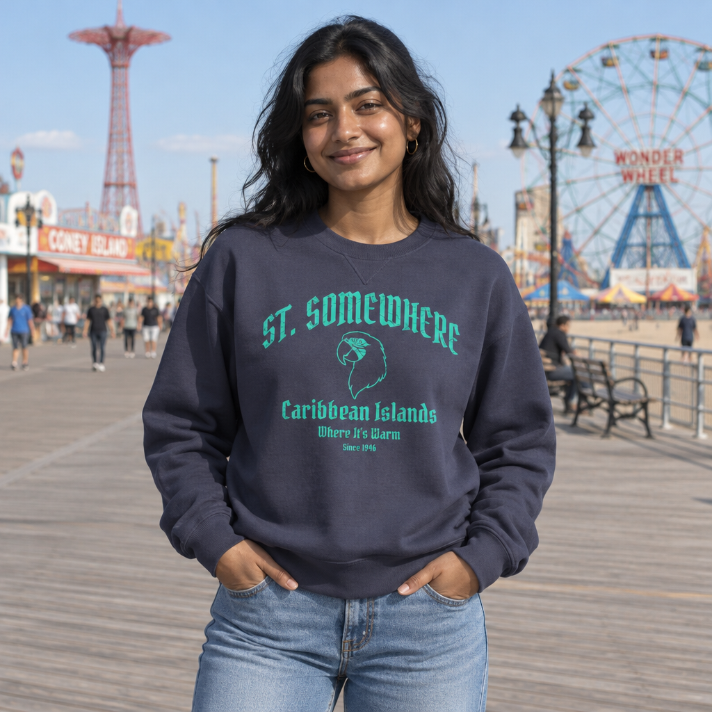 A woman stands on a boardwalk wearing a navy crewneck sweatshirt with a teal graphic that reads 'ST. SOMEWHERE Caribbean Islands Here I'll Bearn' and light blue jeans.
