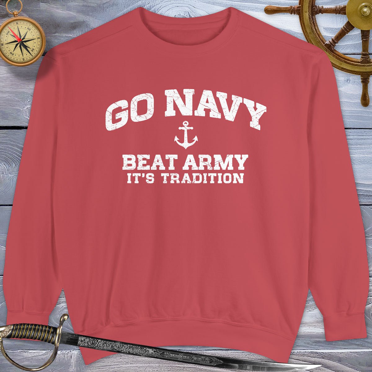 Red Go Navy Sweatshirt with 'Go Navy Beat Army It's Tradition' text on a wooden background with nautical items.