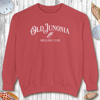 Red sweatshirt with 'Old Junonia' and 'Sheller's Club' text on a wooden surface.