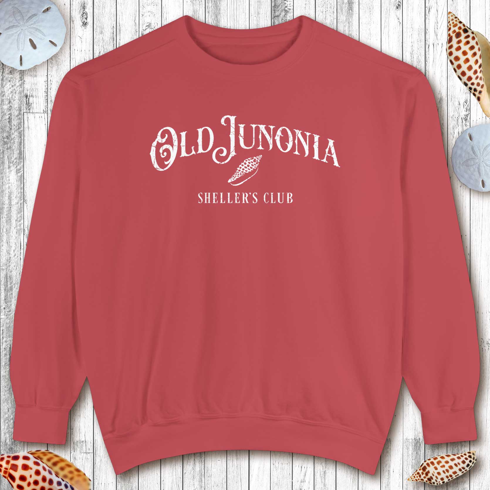 Red sweatshirt with 'Old Junonia' and 'Sheller's Club' text on a wooden surface.