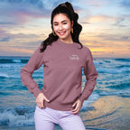 Woman wearing a purple sweatshirt with a logo on a beach at sunset