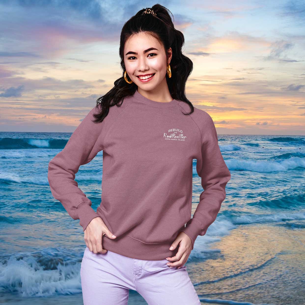 Woman wearing a purple sweatshirt with a logo on a beach at sunset
