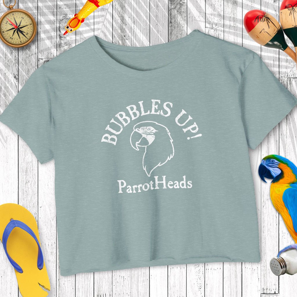 Blue t-shirt with 'Bubbles Up! ParrotHeads' text on a wooden surface with parrot-themed accessories.