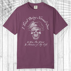A short-sleeve crewneck t-shirt in a dusty plum purple color, featuring a white graphic of a skull wearing a pirate hat with the text 'I Tried Being Normal Once' above and 'It Was The Worst 2 Minutes of My Life' below. The t-shirt is displayed flat against a white wood plank background.