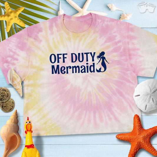 Women's tie-dye crop tee with 'Off Duty Mermaid' design, styled with beach accessories and vibrant colors.