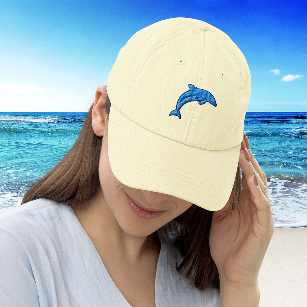 Person wearing a pastel yellow cap with a blue dolphin embroidery on a beach