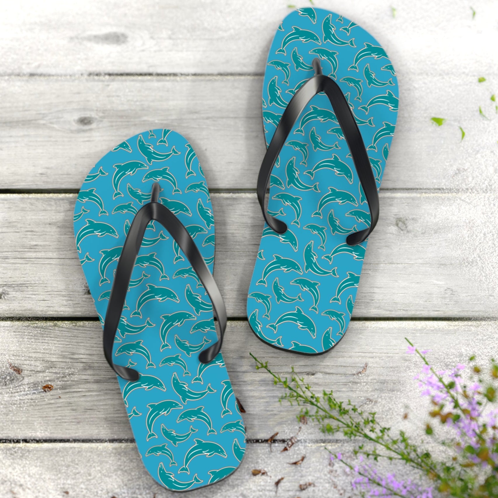 Turquoise Dolphins flip-flops with black straps on a wooden surface with flowers.