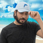 Man wearing a light blue Pastel Dolphin Baseball Hat with an embroidered dolphin logo on a beach