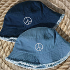 Two bucket hats with peace symbol design on a textured surface