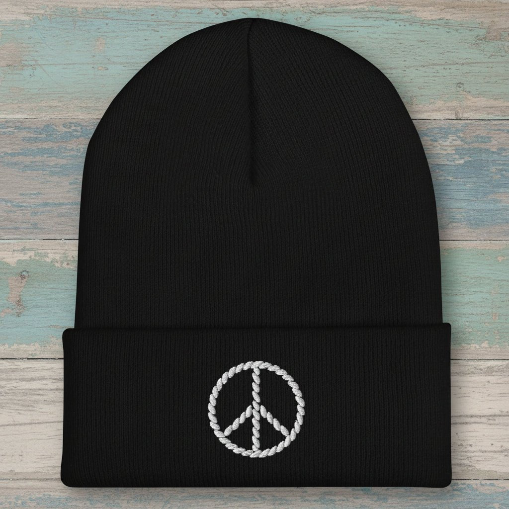 A black ribbed knit beanie hat with a folded cuff, featuring a white embroidered peace sign on the front, set against a plain white background.