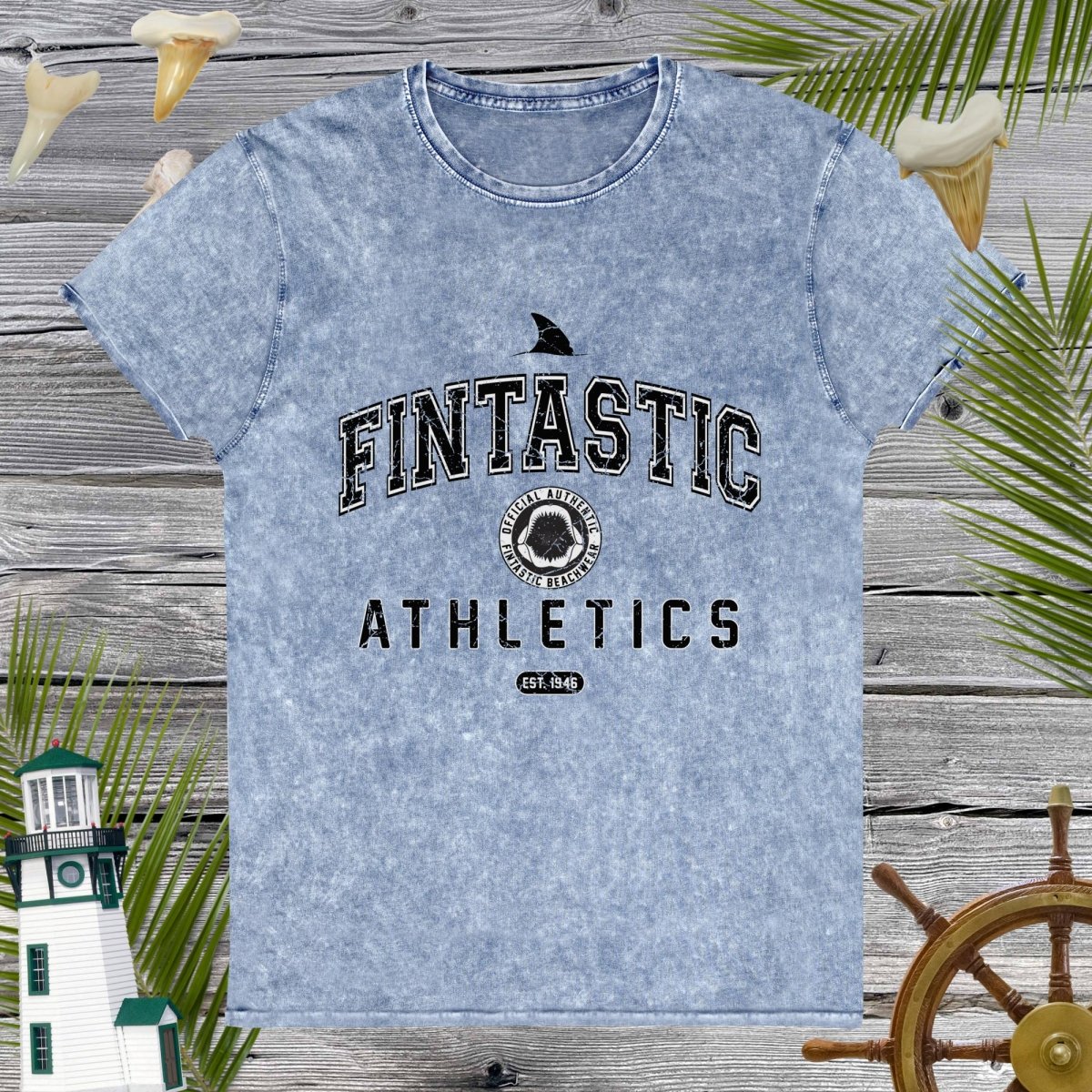 Blue t-shirt with 'Fintastic Athletics' text on a wooden background with decorative elements.