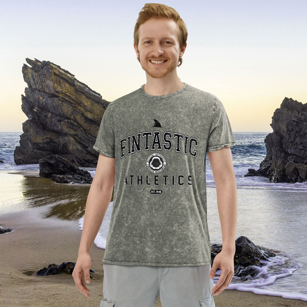 Man wearing a 'Fintastic Athletics' t-shirt on a beach with rocks and ocean in the background