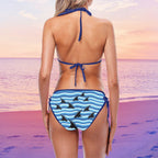 Woman wearing a blue and white striped shark fin bikini with shark design on a beach at sunset.