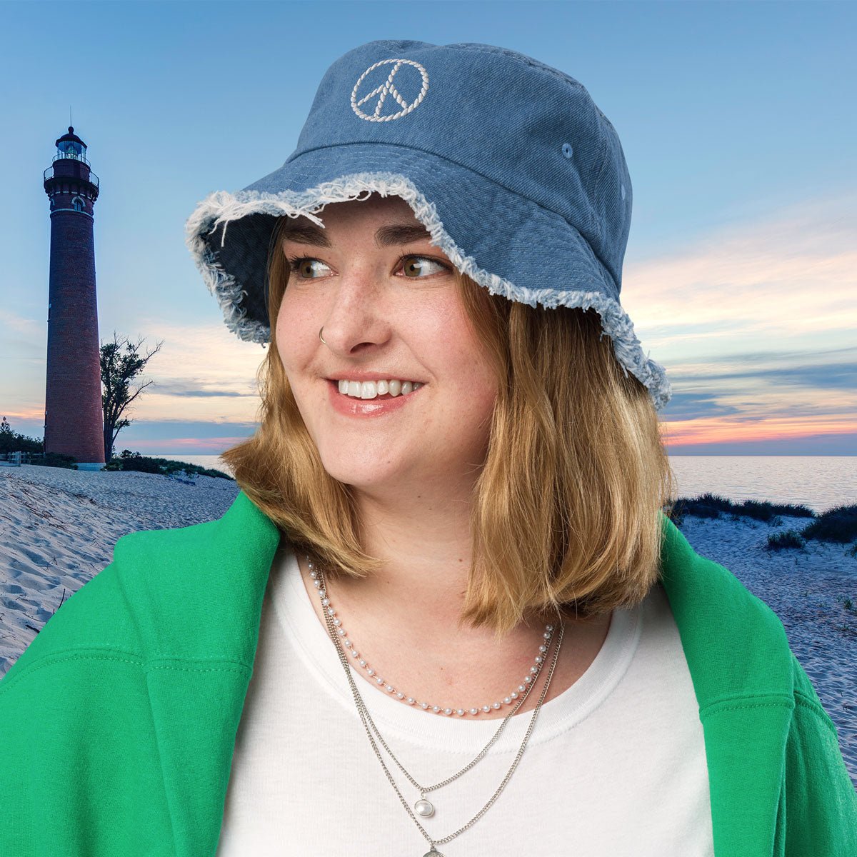 Person wearing a blue bucket hat with a peace symbol on a beach with a lighthouse in the background.