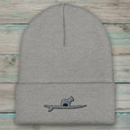 A light gray ribbed knit beanie hat with a folded cuff, featuring a small embroidered graphic of a frenchie standing on a surfboard on the front cuff.