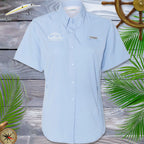 Light blue short-sleeve shirt with brand logos on a wooden background with decorative elements.