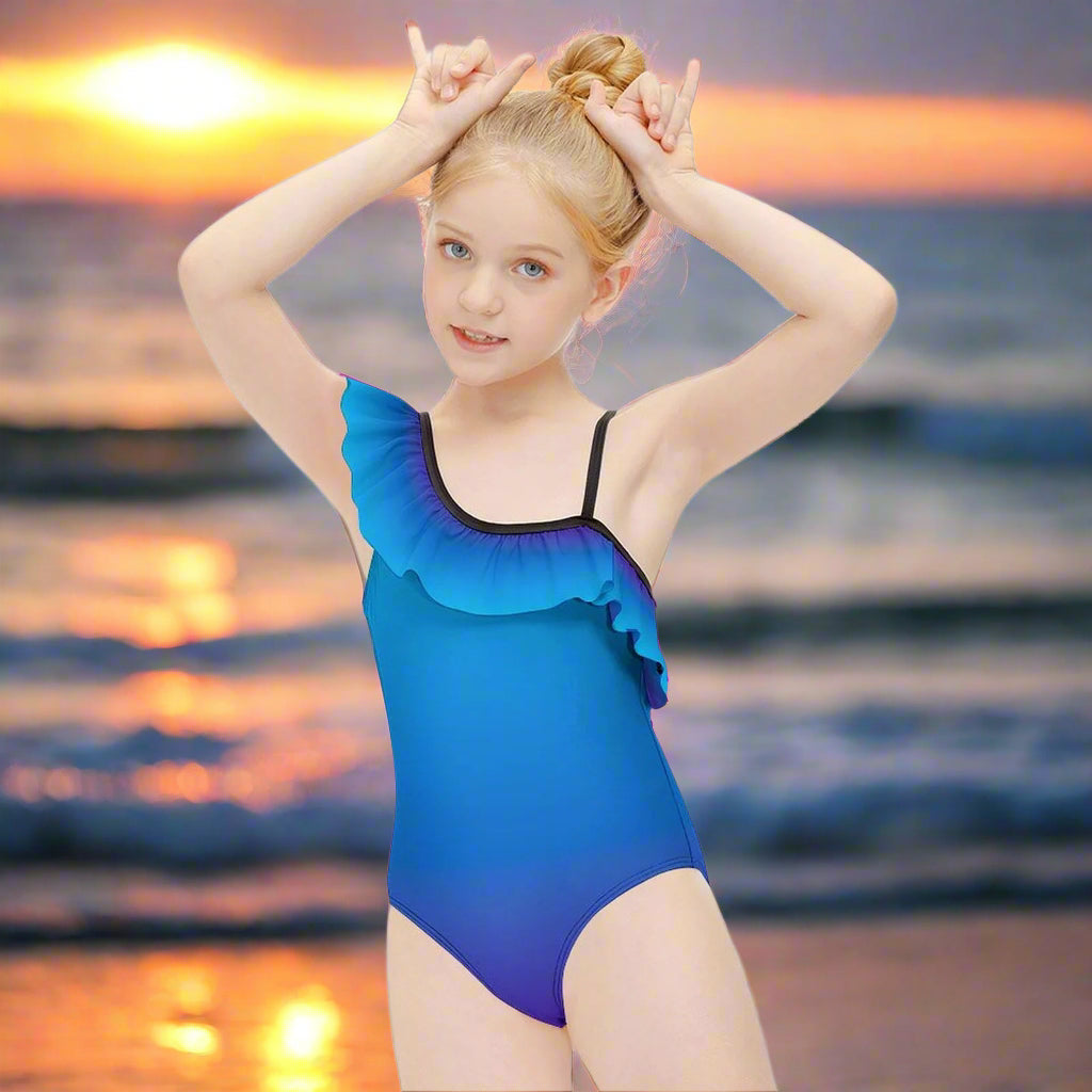 Young girl wearing a blue ombré swimsuit with ruffles flashes the shaka sign on a beach at sunset