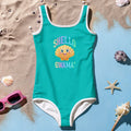 Green swimsuit with 'Shello Gwama' text and shell graphic on sand with shells and sunglasses.