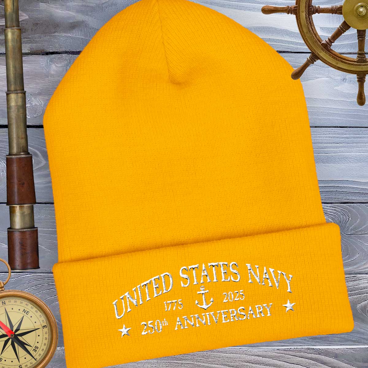 Yellow beanie with 'United States Navy 250th Anniversary' text on a wooden background with nautical items.