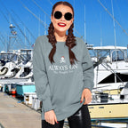 Woman wearing a sweatshirt with a graphic design and text, standing in front of boats at a dock.