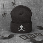 Black beanie with a logo on a textured gray background with Halloween decorations.