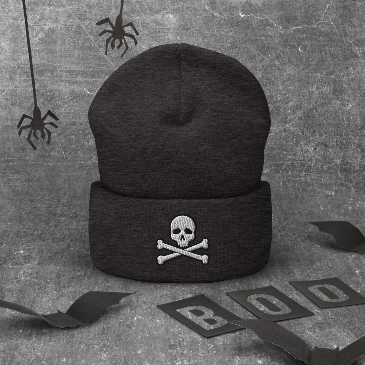Black beanie with a logo on a textured gray background with Halloween decorations.