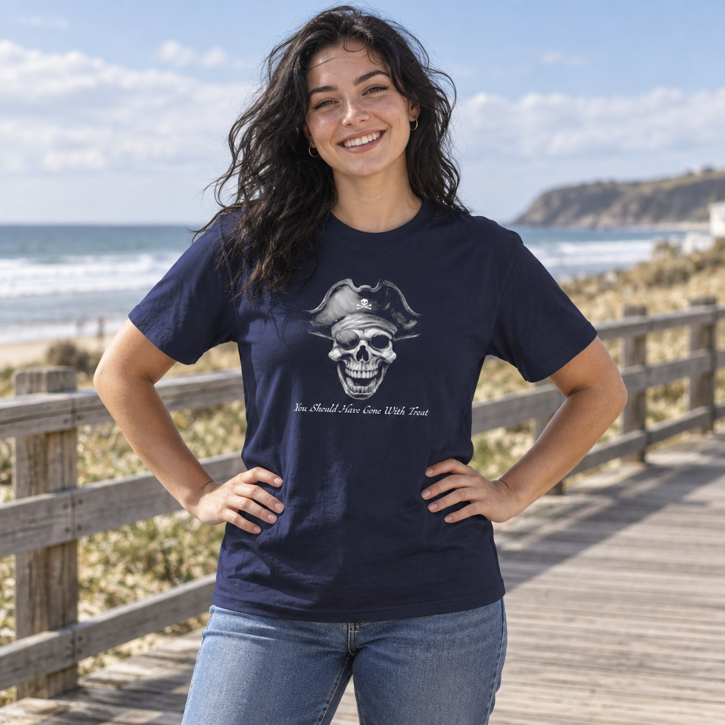 A woman stands on a wooden boardwalk by the beach wearing a navy blue graphic t-shirt with a pirate skull design and blue jeans.