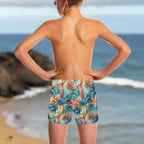 Teen boy wearing colorful tropical surf themed swim shorts, looking out over the pacific ocean in Hawaii