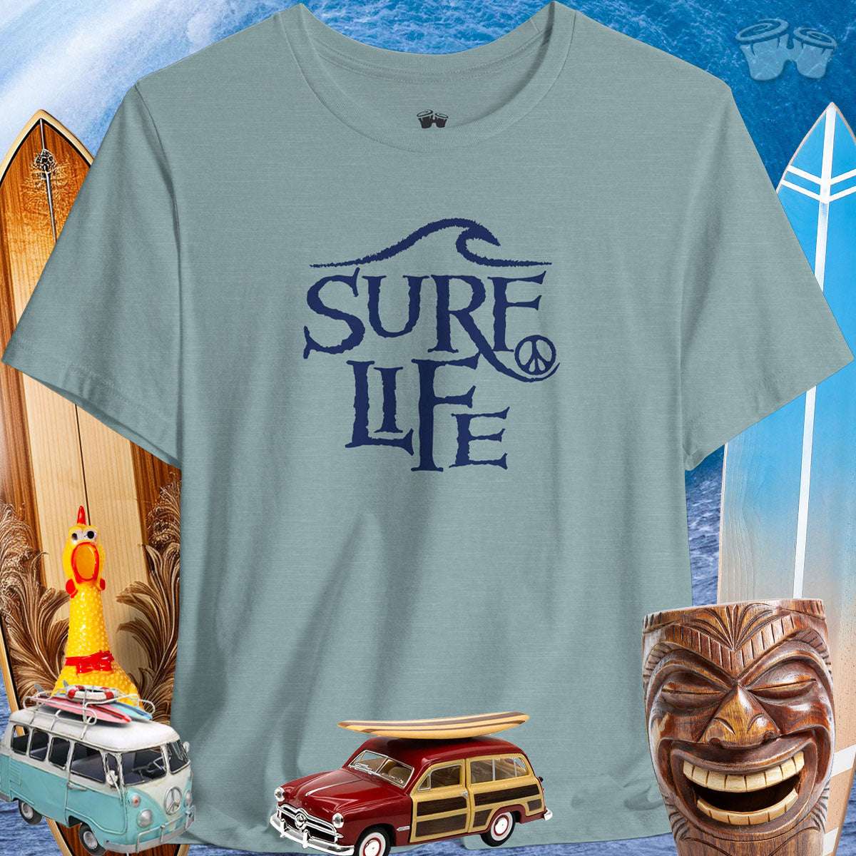 Surfer Life Tee in aqua, surrounded by vintage surfboards and tiki decor, embodying beach vibes and adventurous spirit.