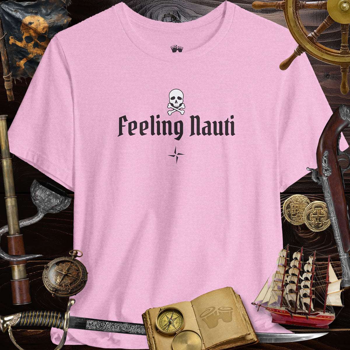 Feeling Nauti' Skull & Crossbone Unisex Pirate Tee in pink, surrounded by nautical treasures and pirate gear.