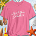 Pink unisex tee with 'Shell Yeah Beaches' design, surrounded by seashells and beach-themed decor.