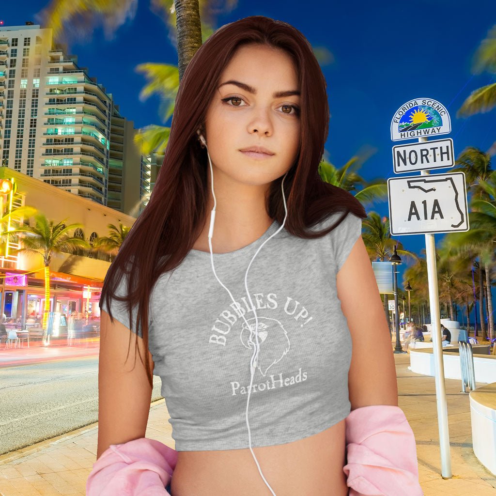 Woman wearing a heather gray ParrotHead Crop Top with Bubbles Up text, standing in front of a cityscape with palm trees and an A1A street sign.