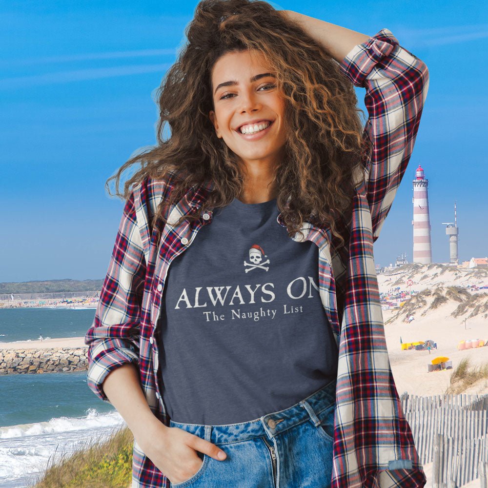 Woman wearing a navy t-shirt with text and a skull design, standing by the ocean with a lighthouse in the background.