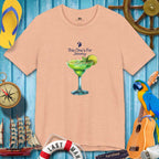 Beige t-shirt with a cocktail graphic and text on a blue wooden background with tropical items.