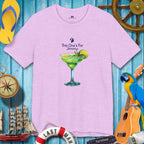 Purple t-shirt with a cocktail graphic and text on a blue wooden background with tropical items.