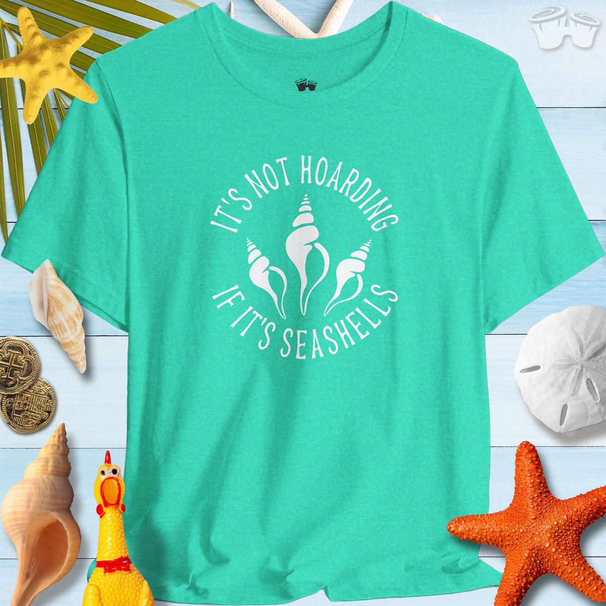 Beach Lover's Unisex Tee in teal with 'It's Not Hoarding If It's Seashells' print, surrounded by seashells and beach decor.