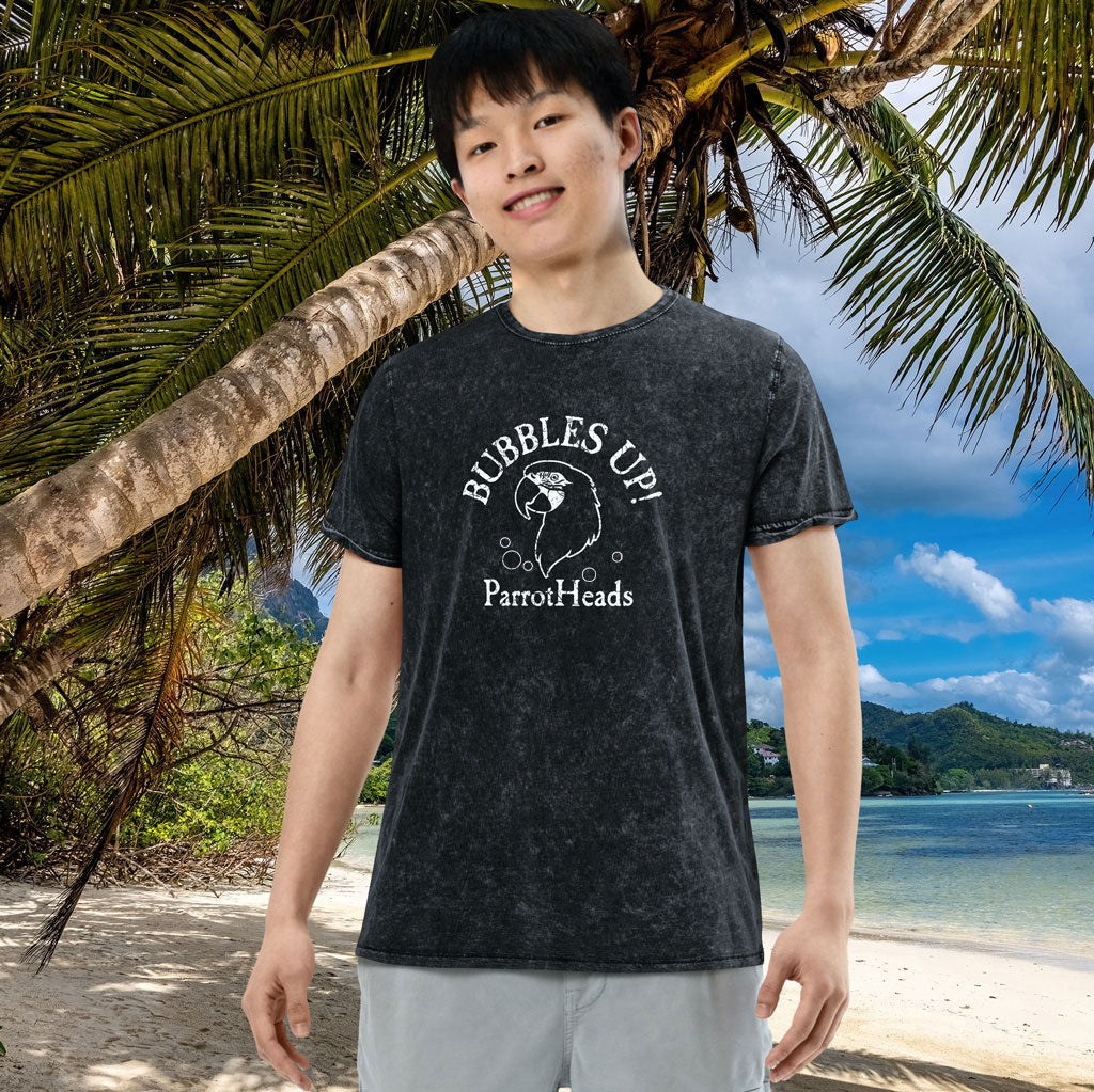 Person wearing a black t-shirt with 'Bubbles Up! ParrotHeads' text on a beach with palm trees and ocean in the background