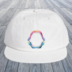 A white baseball cap with a colorful shark mouth graphic on the front, displayed on a gray wooden plank surface.