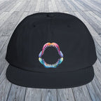 A navy flat-brim surf hat with a colorful shark-mouth graphic on the front, displayed on a gray wooden plank surface.