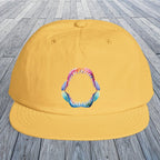 A sunset yellow baseball cap with a colorful shark teeth graphic on the front, displayed on a gray wooden plank surface.