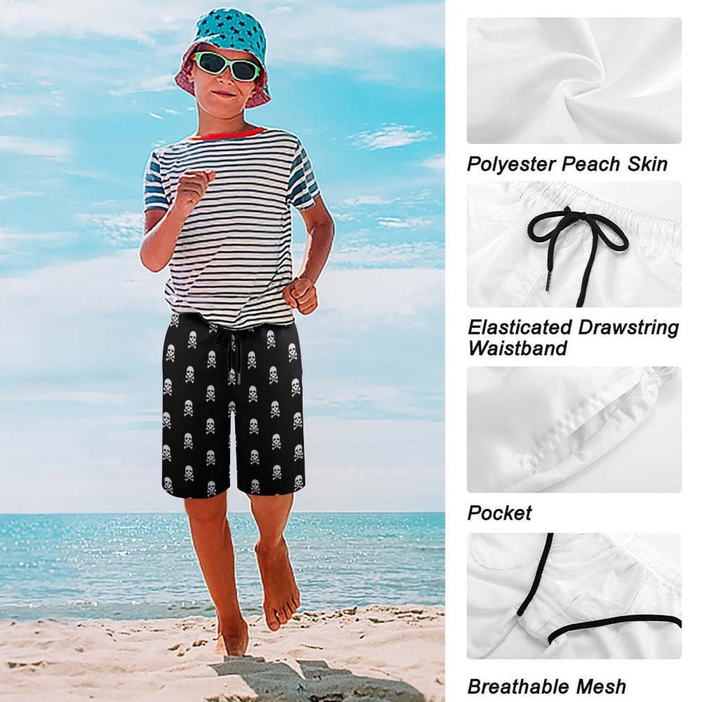 Child wearing a striped shirt, bucket hat, sunglasses, and black shorts with skull patterns on a beach.