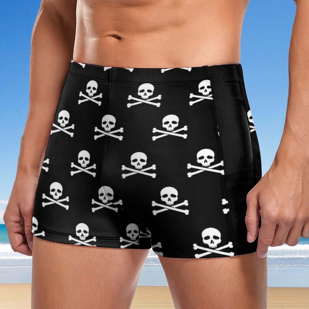 Person wearing black swim shorts with skull and crossbones pattern on a beach.