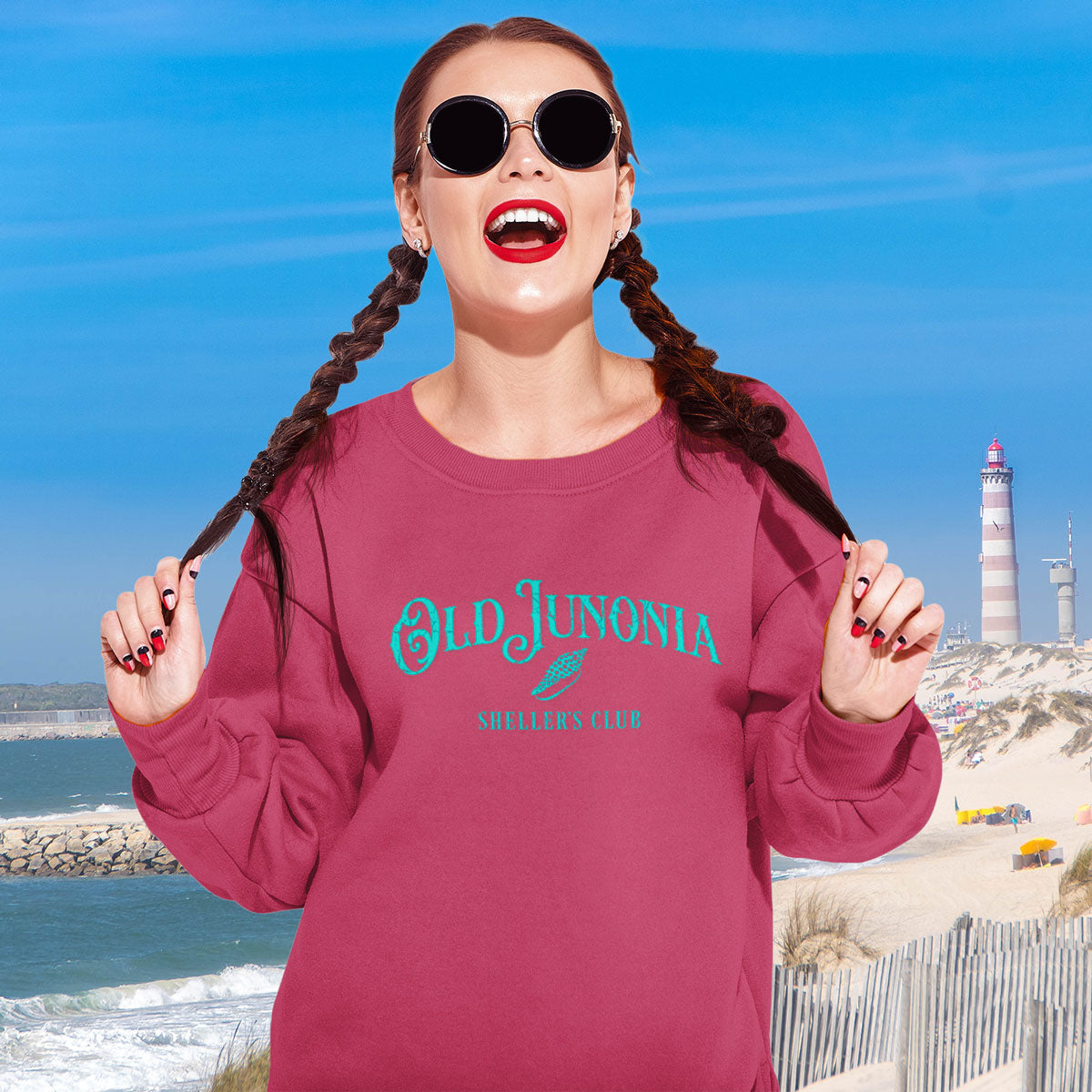 Woman wearing a pink sweatshirt with 'Old Junonia' text at the beach