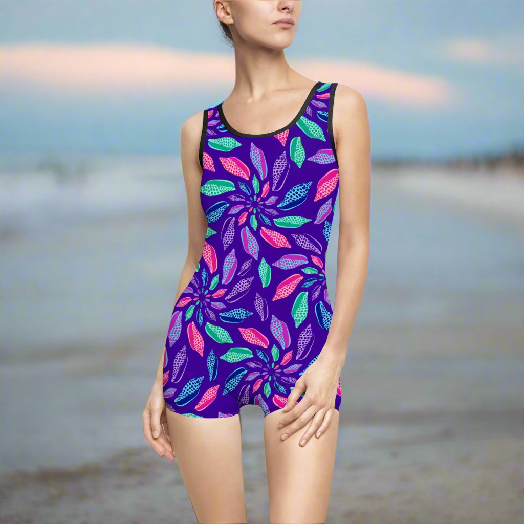 Model sporting brilliantly colored Junonia Seashells Pattern on a vintage one piece swimsuit with black trim standing on beach looking for to find her fist Junonia