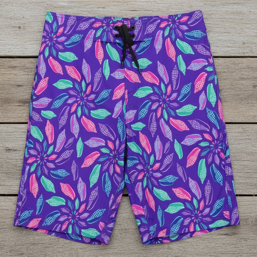 Purple board shorts with colorful junonia seashell pattern on a rustic wood background