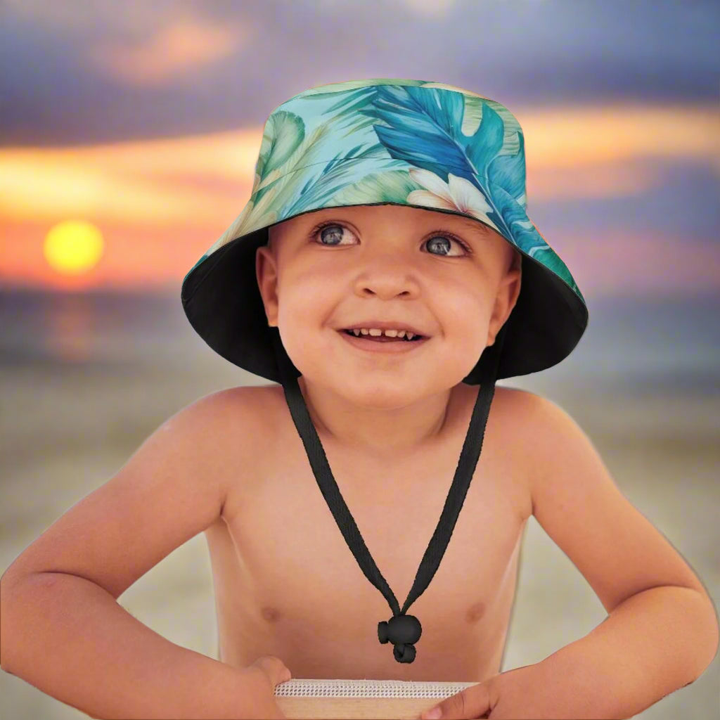 Child wearing a tropical leaf patterned sun hat with a beach background