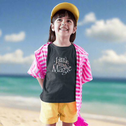 Child wearing a 'Little Miss Magic' shirt with a pink cape and yellow shorts on St. Pete Beach